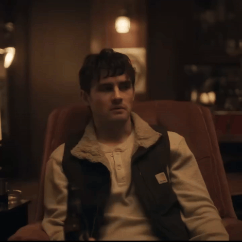 A Man Sitting In A Chair Wearing A Carhartt Vest GIF
