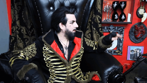 A Man Sitting In A Chair With A Black And Gold Jacket On GIF
