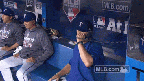 A Man Sitting In A Dugout Talking On A Phone With Mlb.com Written On The Wall Behind Him GIF