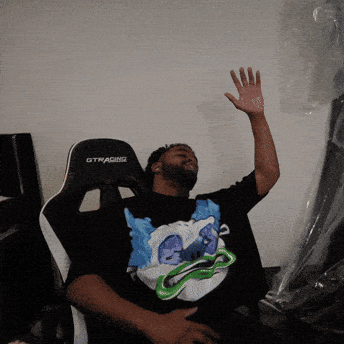 A Man Sitting In A Gtracing Chair With His Hand Up GIF
