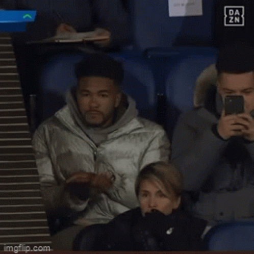 A Man Sitting In A Stadium Looking At His Phone With A Da Zn Logo In The Background GIF