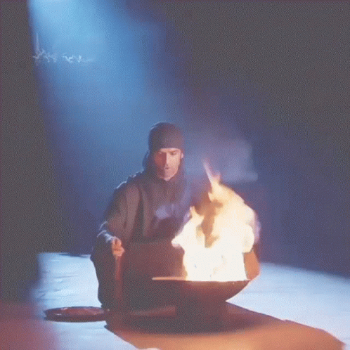 A Man Sitting In Front Of A Bowl Of Fire With Smoke Coming Out Of It GIF