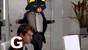 A Man Sitting In Front Of A Computer With A Cat Mascot Behind Him With The Letter G In The Foreground GIF