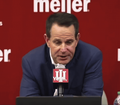 A Man Sitting In Front Of A Meijer Sign Talking Into A Microphone GIF