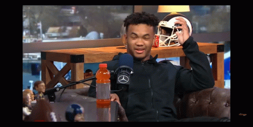 A Man Sitting In Front Of A Microphone Holding A Football Helmet And A Gatorade Bottle GIF
