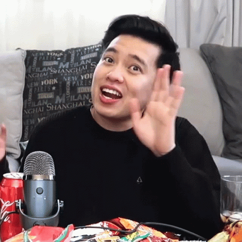A Man Sitting In Front Of A Microphone In Front Of A Pillow That Says Milan On It GIF