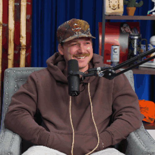 A Man Sitting In Front Of A Microphone Wearing A Hat That Says ' Abercrombie & Fitch ' On It GIF