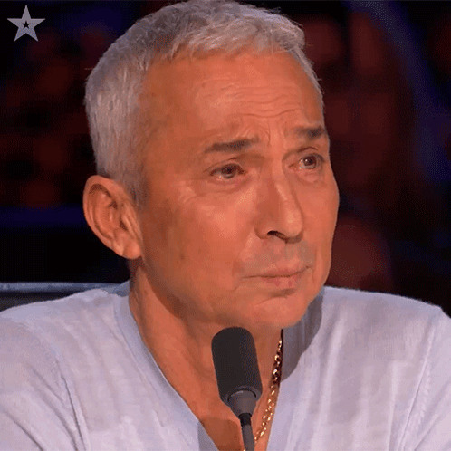 A Man Sitting In Front Of A Microphone With A Star In The Upper Right Corner GIF
