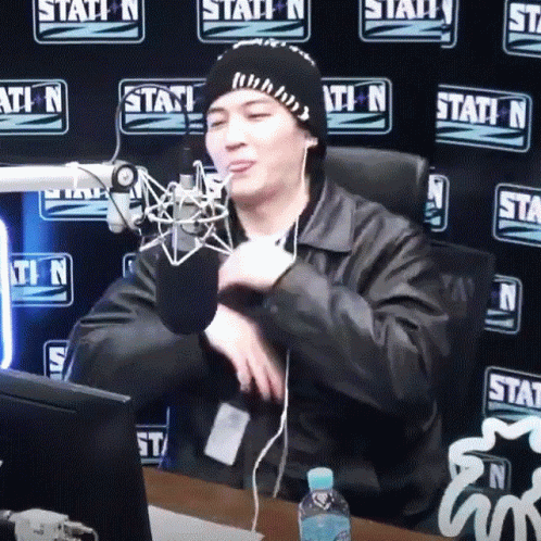 A Man Sitting In Front Of A Microphone With A Station N Wall Behind Him GIF