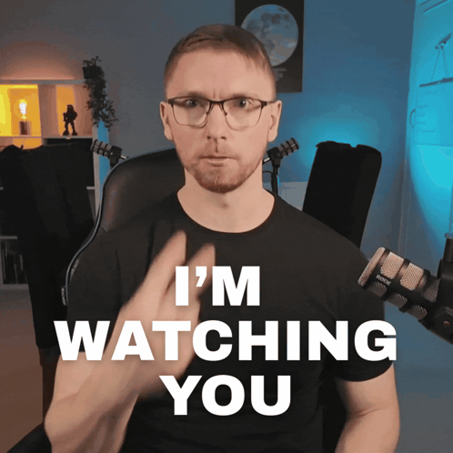 a man sitting in front of a microphone with the words i 'm watching you behind him