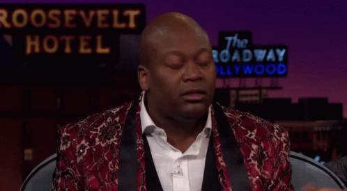 A Man Sitting In Front Of A Roosevelt Hotel Sign With His Hands In The Air GIF