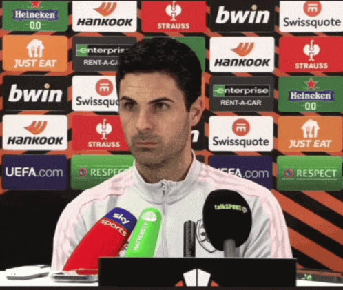 A Man Sitting In Front Of A Row Of Advertisements Including Bwin Swissquote And Heineken GIF