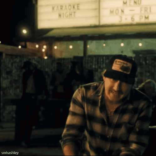 A Man Sitting In Front Of A Sign That Says " Karaoke Night " GIF