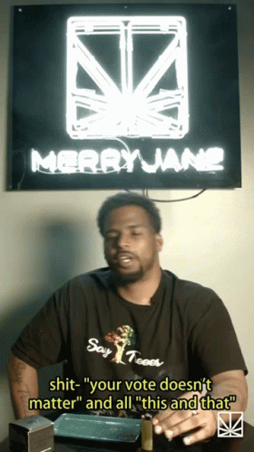A Man Sitting In Front Of A Sign That Says Merryjane On It GIF