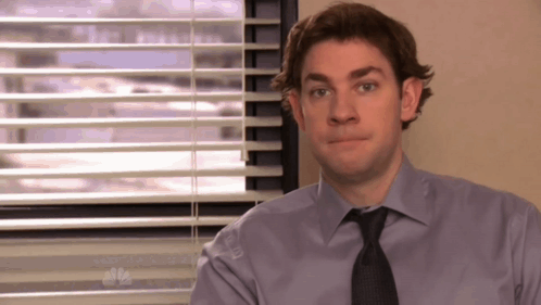 A Man Sitting In Front Of A Window With Blinds And A Nbc Logo GIF
