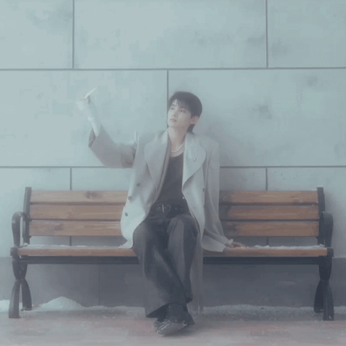 A Man Sitting On A Bench With His Hand Up GIF