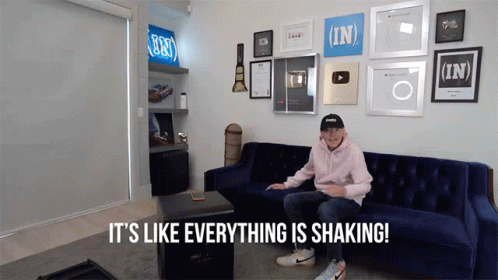 A Man Sitting On A Blue Couch With The Words It 'S Like Everything Is Shaking Behind Him GIF