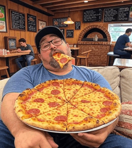 A Man Sitting On A Couch Eating A Large Pizza GIF