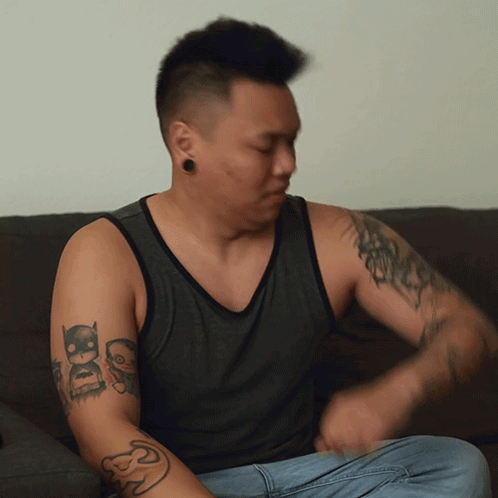 A Man Sitting On A Couch Has A Tattoo On His Arm That Says Dc GIF