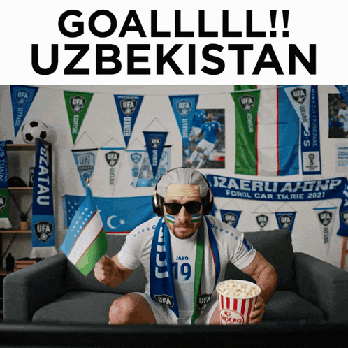 A Man Sitting On A Couch Holding A Bag Of Popcorn And Wearing A Scarf That Says Ufa GIF