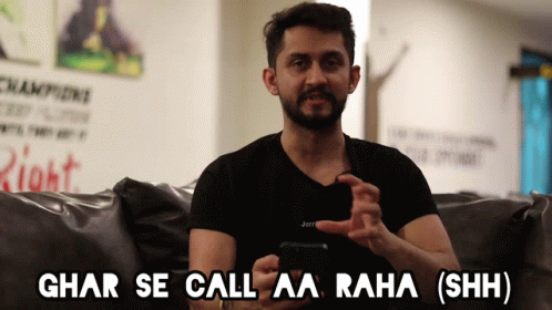 A Man Sitting On A Couch Holding A Cell Phone With The Words Ghar Se Call Aa Raha Shh GIF