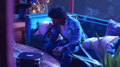 A Man Sitting On A Couch Holding A Microphone GIF