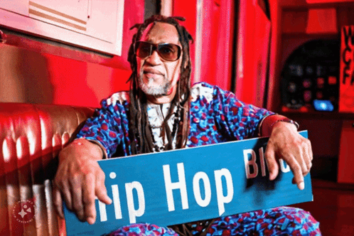 A Man Sitting On A Couch Holding A Sign That Says Hip Hop Blvd. GIF