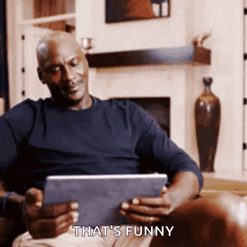 A Man Sitting On A Couch Looking At A Tablet With The Words That 'S Funny Below Him GIF