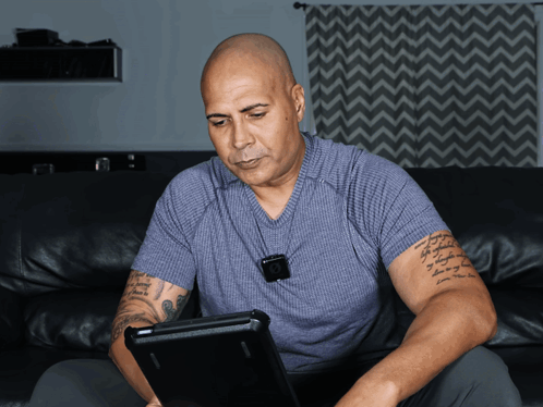 a man sitting on a couch using a laptop with a tattoo on his arm