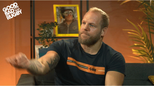 A Man Sitting On A Couch Wearing A Shirt That Says Gbr On It GIF