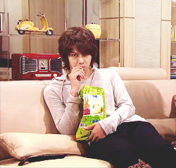 A Man Sitting On A Couch With A Bag Of Chips In His Hand GIF