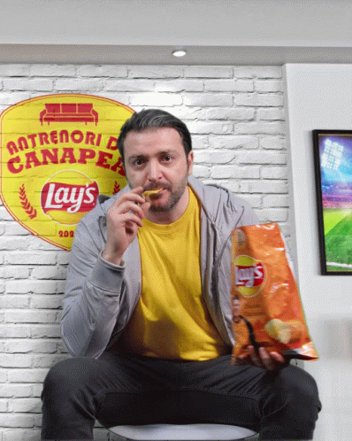A Man Sitting On A Couch With A Bag Of Lays Chips GIF