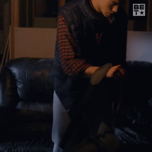 A Man Sitting On A Couch With A Be T Logo On The Wall Behind Him GIF