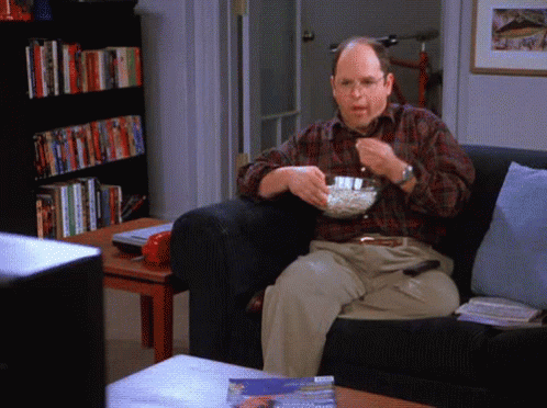 A Man Sitting On A Couch With A Bowl Of Popcorn In His Hand GIF