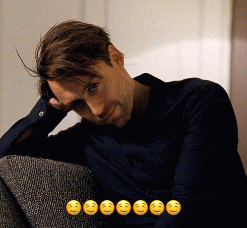 A Man Sitting On A Couch With A Bunch Of Smiley Faces Behind Him GIF
