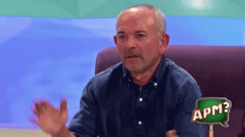A Man Sitting On A Couch With A Sign That Says Apm GIF