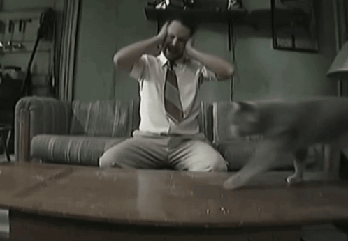 A Man Sitting On A Couch With His Hands On His Head GIF