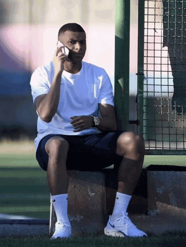 A Man Sitting On A Ledge Talking On A Cellphone GIF