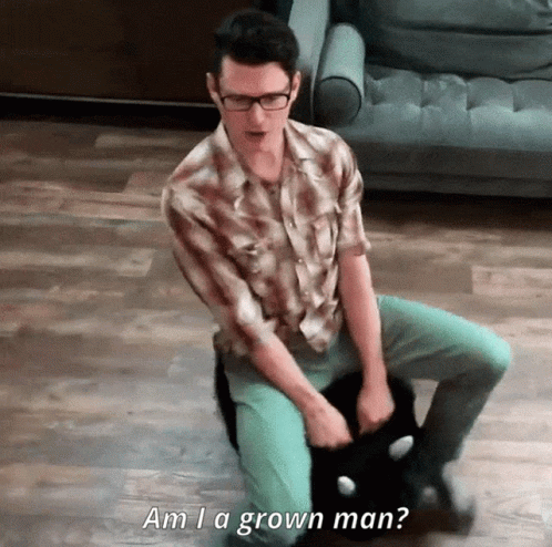 A Man Sitting On The Floor Holding A Cat With The Words Am I A Grown Man Written Below Him GIF