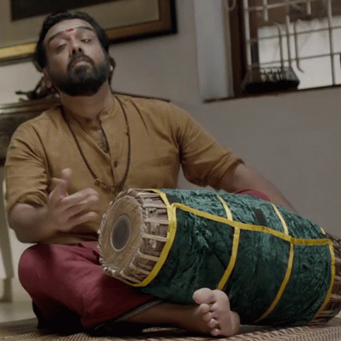 A Man Sitting On The Floor Playing A Drum GIF