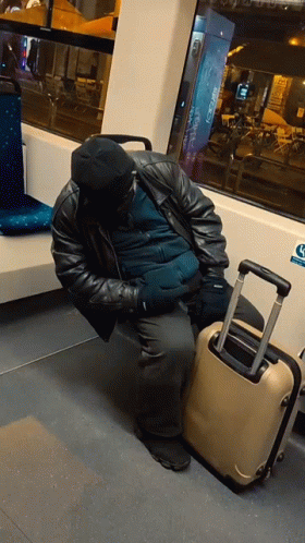 A Man Sleeping On A Bus Next To A Suitcase With A Sticker On The Wall That Says ' Handicap ' GIF