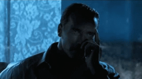 A Man Smoking A Cigarette In A Dark Room With A Blue Background GIF