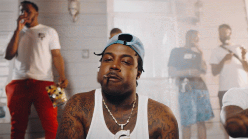 A Man Smoking A Cigarette In Front Of A Group Of Men GIF