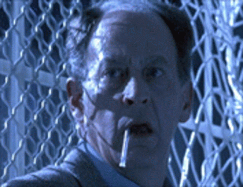 A Man Smoking A Cigarette In Front Of A Wire Fence GIF