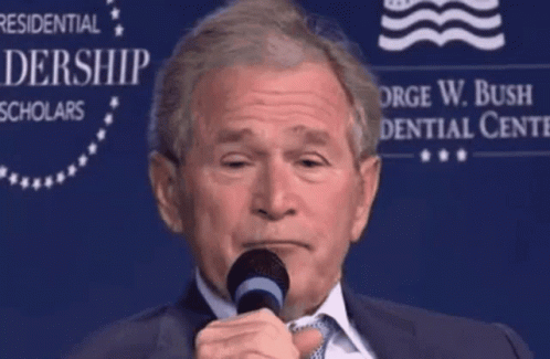 A Man Speaking Into A Microphone In Front Of A Sign That Says George W. Bush Presidential Center GIF