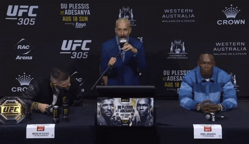 A Man Speaking Into A Microphone In Front Of A Ufc 305 Banner GIF
