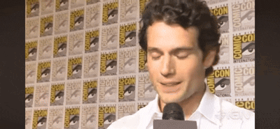 A Man Speaking Into A Microphone In Front Of A Wall That Says Comic Con On It GIF