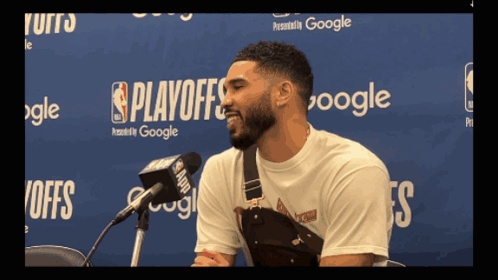 a man speaking into a microphone in front of a wall that says playoffs on it