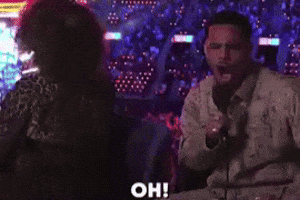 A Man Speaking Into A Microphone While A Woman Stands Behind Him With The Word Oh Written On The Bottom GIF
