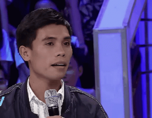 A Man Speaking Into A Microphone With A Crowd Behind Him GIF